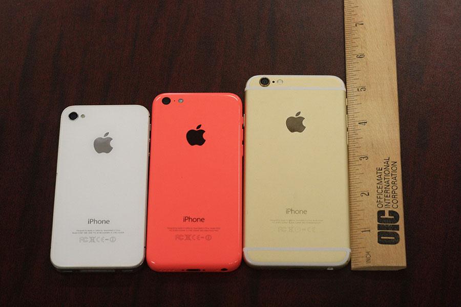 The IPhone 6, the IPhone 5c, and the IPhone 4 are all lined up to compare the width and size of the different versions. The IPhone 6 is the gold, the Iphone 5c is the pink, and the IPhone 4 is the white.