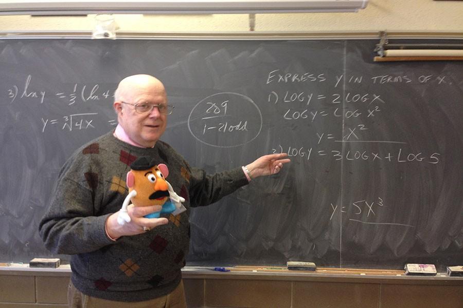 Calculus+teacher+George+Appleby+poses+with+one+of+his+cherished+Mr.+Potatoheads+at+his+board.+Appleby+has+been+a+devoted+math+teacher+at+John+Carroll+for+43+years.+%0A