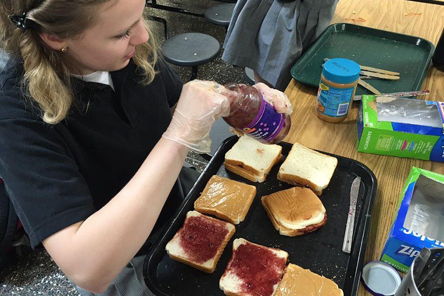 Junior Anna Smith makes peanut butter and jelly sandwiches as part of a service opportunity organized by the Service Club. The Service Club made 20 loaves worth of peanut butter and jelly sandwiches which they gave to the soup kitchen, Our Daily bread.