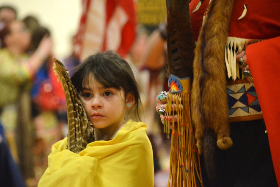 A little girl holds onto a feather and her blanket while walking around the dance circle.