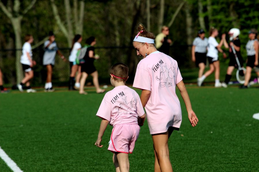 Seven-year-old Mia Cochran and senior Charlotte Haggerty hold hands as they walk across the field before the game. Mia joined the womens varsity lacrosse team on the sidelines during the game and cheered on the team.